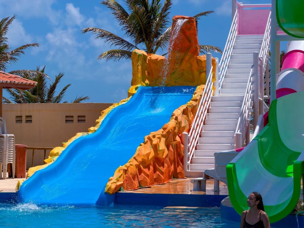 Un tobogán de agua con diseño rocoso, una escalera y una zona de piscina.