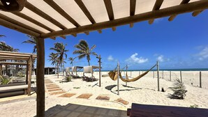 Een terras aan het strand met een hangmat, palmbomen en een houten pergola.