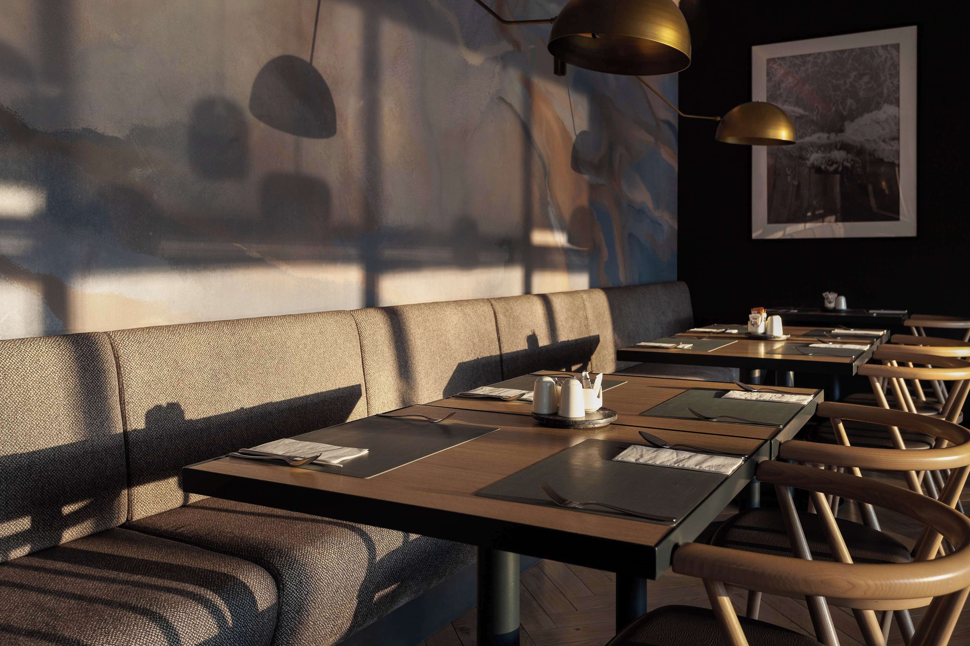 A restaurant interior with wooden tables, cushioned booths, and pendant lighting.