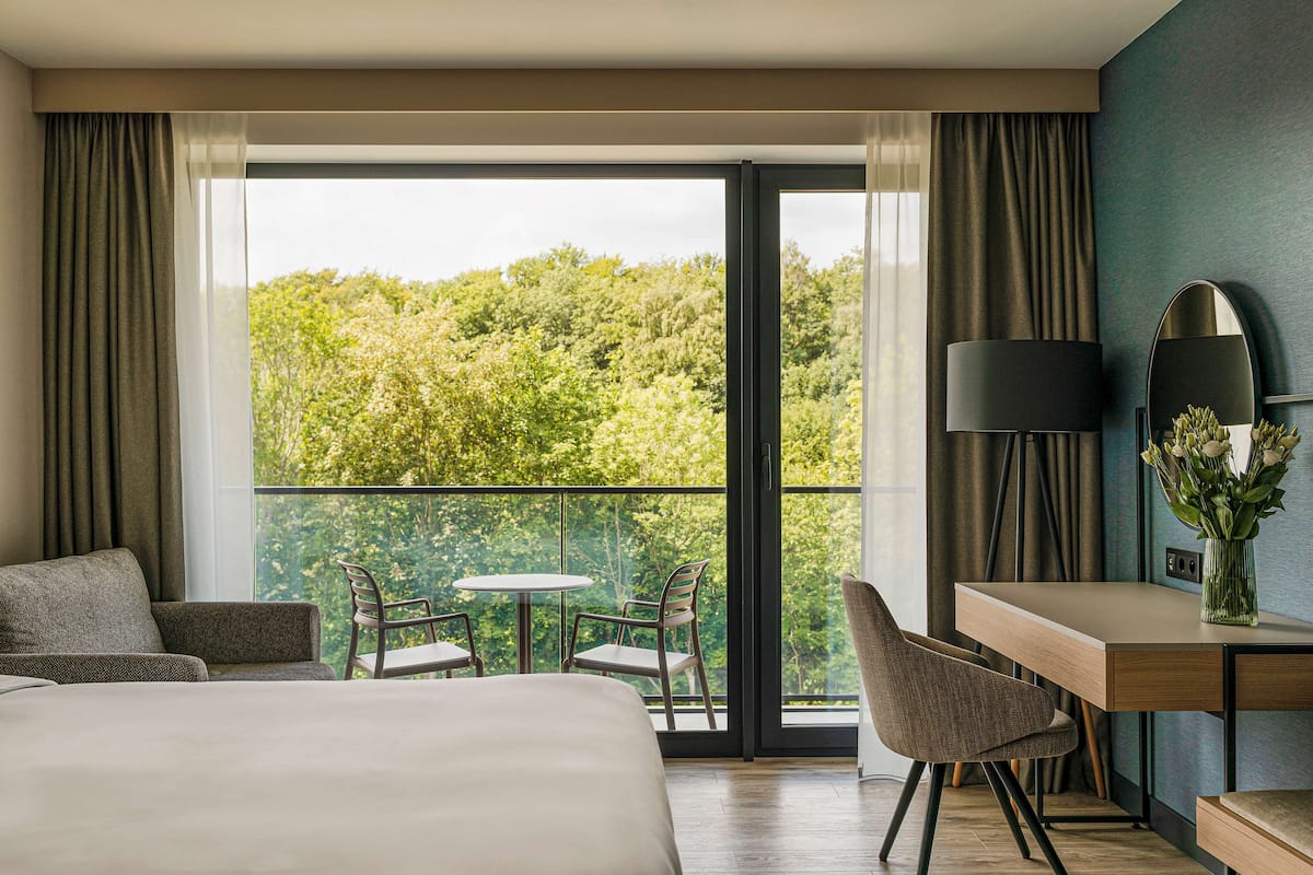 A hotel room with a large balcony, a bed, a desk, and a chair.