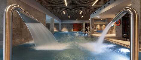 Una piscina interior moderna con borde inclinado, techo de madera y un flotador en la pared.
