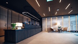 Een moderne receptie met een donker receptiebalie, een potplant en twee zithoeken met lampen.