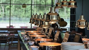 Een modern restaurant met een lange toonbank, meerdere hangende lampen en uitzicht op groen buiten.