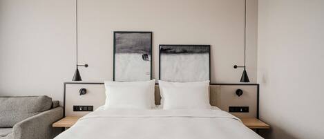 A modern bedroom with a large bed, two bedside tables with lamps, and two framed artworks on the wall.