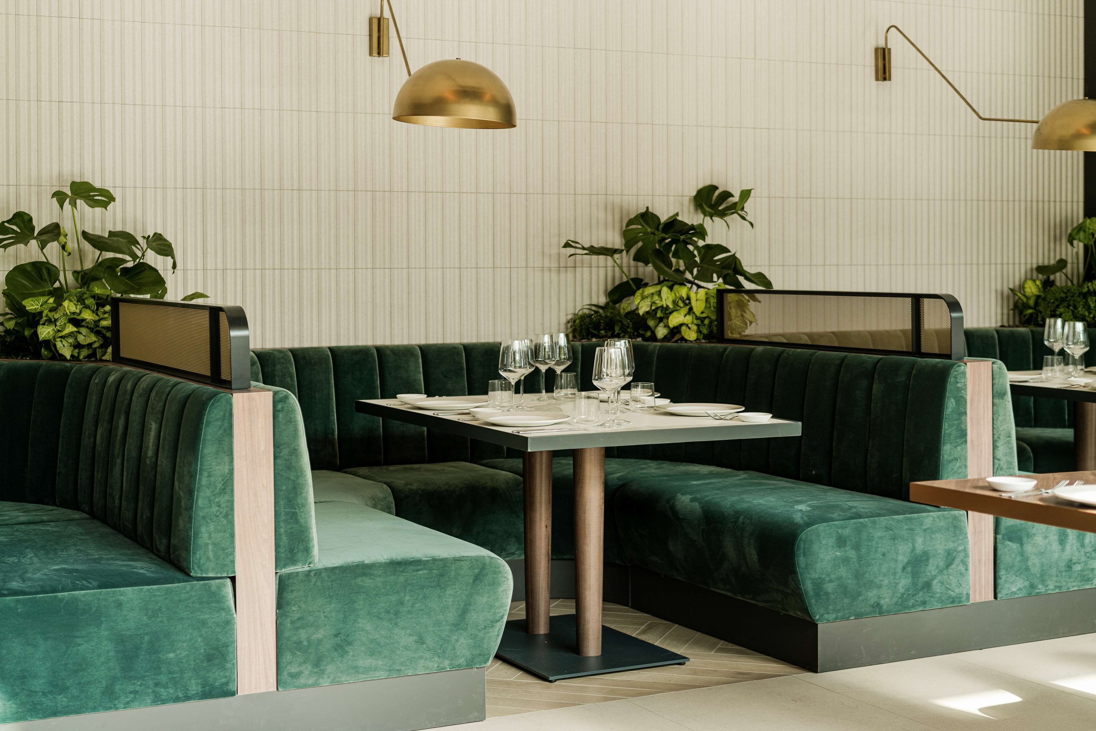 Een restaurant met groen bekleden zitjes, een houten tafel en een wand met een rasterpatroon.