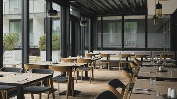 Un restaurant moderne avec des tables et des chaises en bois, de grandes fenêtres et des lampes suspendues.