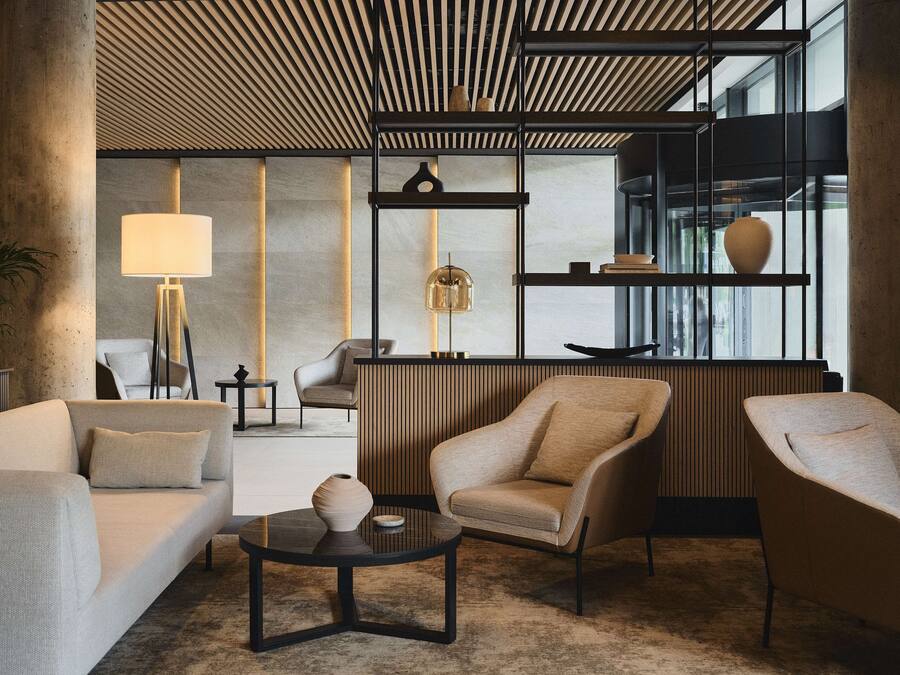 Un salon moderne avec un canapé, des fauteuils, une table basse et une lampe. Une grande fenêtre offre une vue sur l’extérieur.