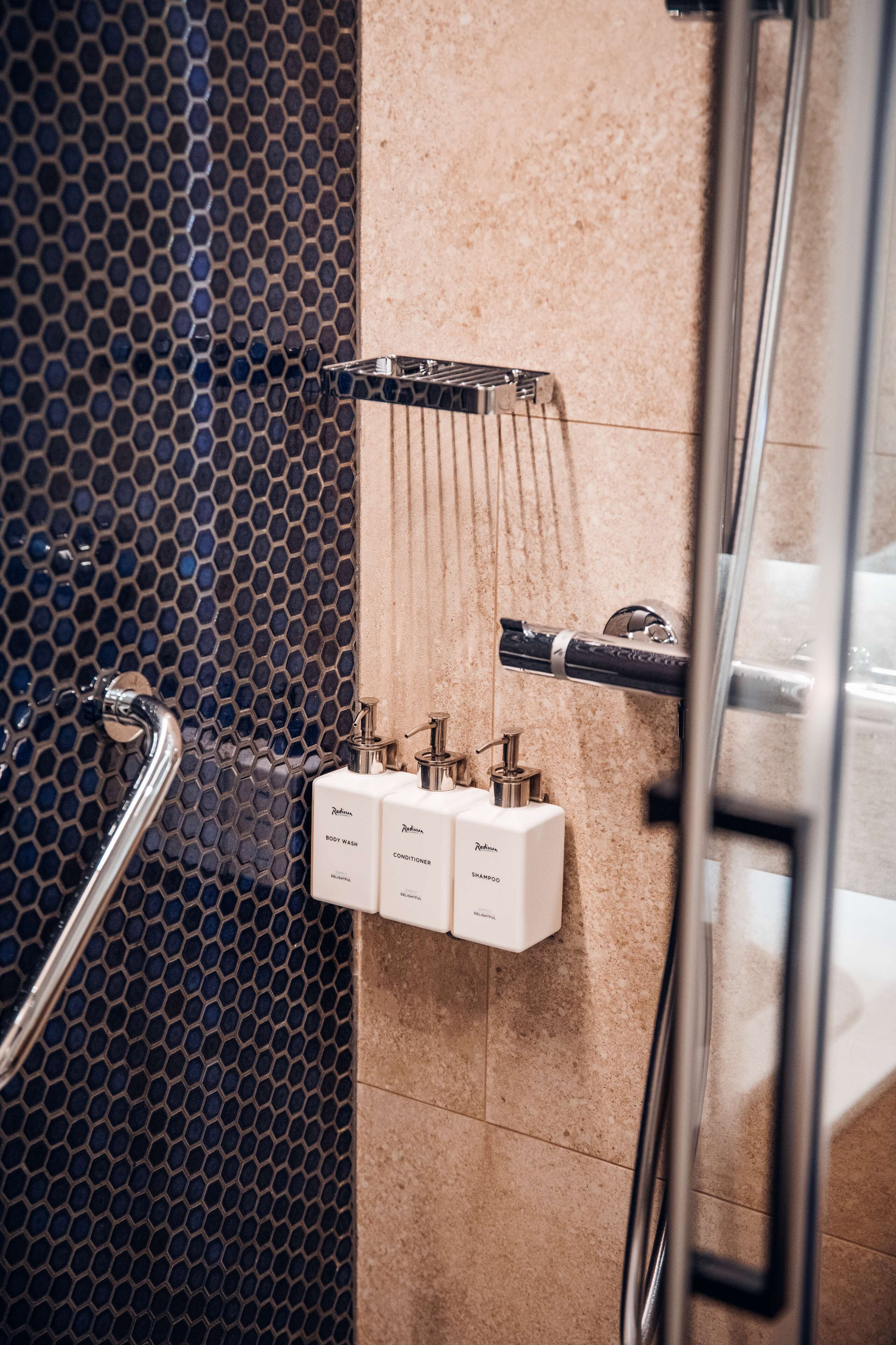 Une salle de bain équipée d’une douche, d’un sèche-mains et de trois bouteilles de shampoing et d’après-shampoing.