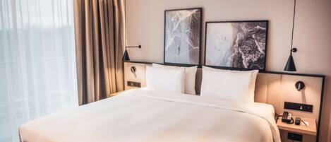 A hotel room with a large bed, a bedside table with a lamp, and two framed pictures on the wall.