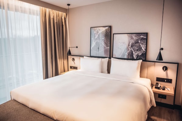 Una habitación de hotel con una cama grande, una mesita de noche con lámpara y dos cuadros en la pared.