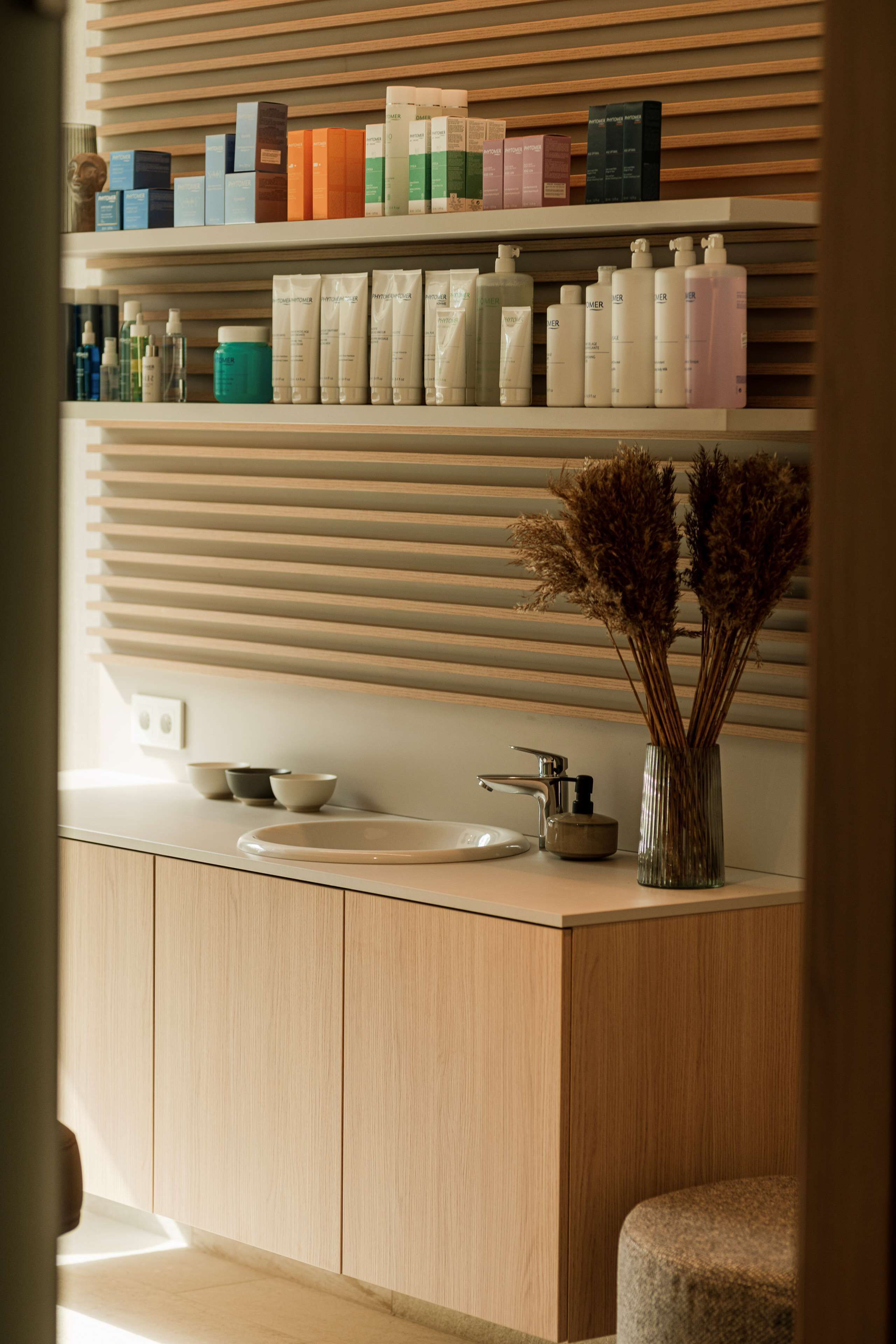A modern bathroom with a wooden vanity, a sink, and a shelf with various toiletries.