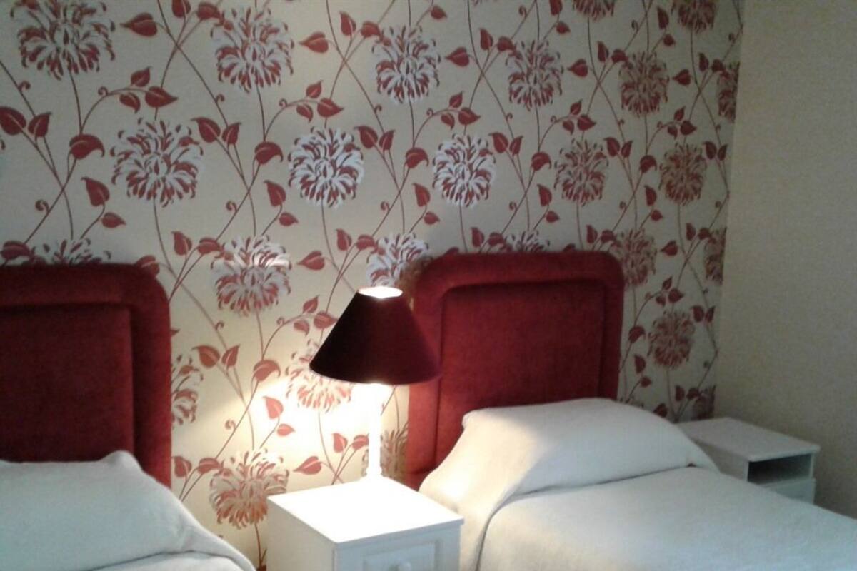 Een hotelkamer met twee bedden, een nachtkastje met een lamp en bloemenbehang.