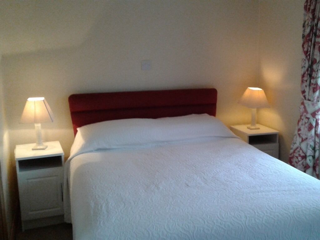 A neatly made bed with white linens in a room with a red headboard. There are two bedside tables, each with a lamp.
