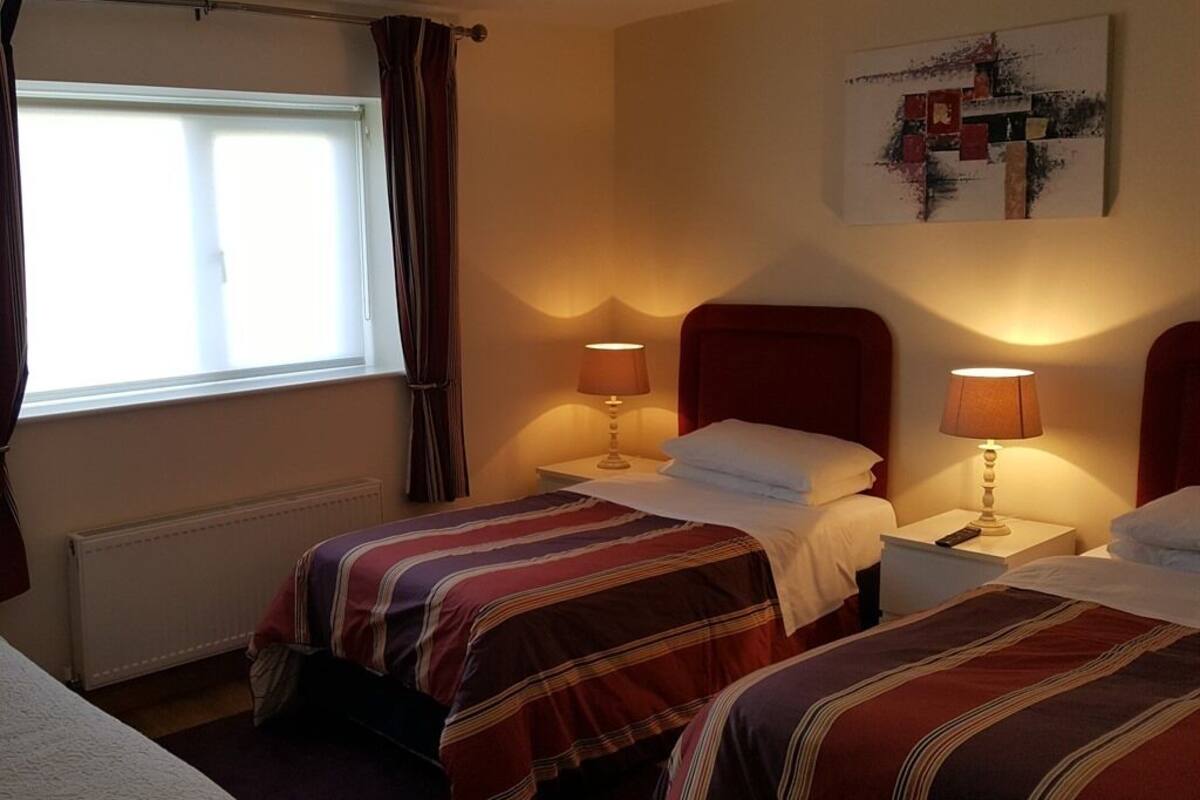 Een hotelkamer met twee bedden, elk met een rode hoofdbord, een raam met gordijnen en twee bedlampen.