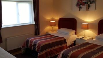 A hotel room with two beds, each with a red headboard, a window with curtains, and two bedside lamps.