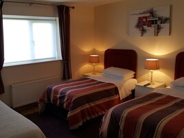 Habitación de hotel con dos camas, cada una con cabecero rojo, una ventana con cortinas y dos lámparas de noche.