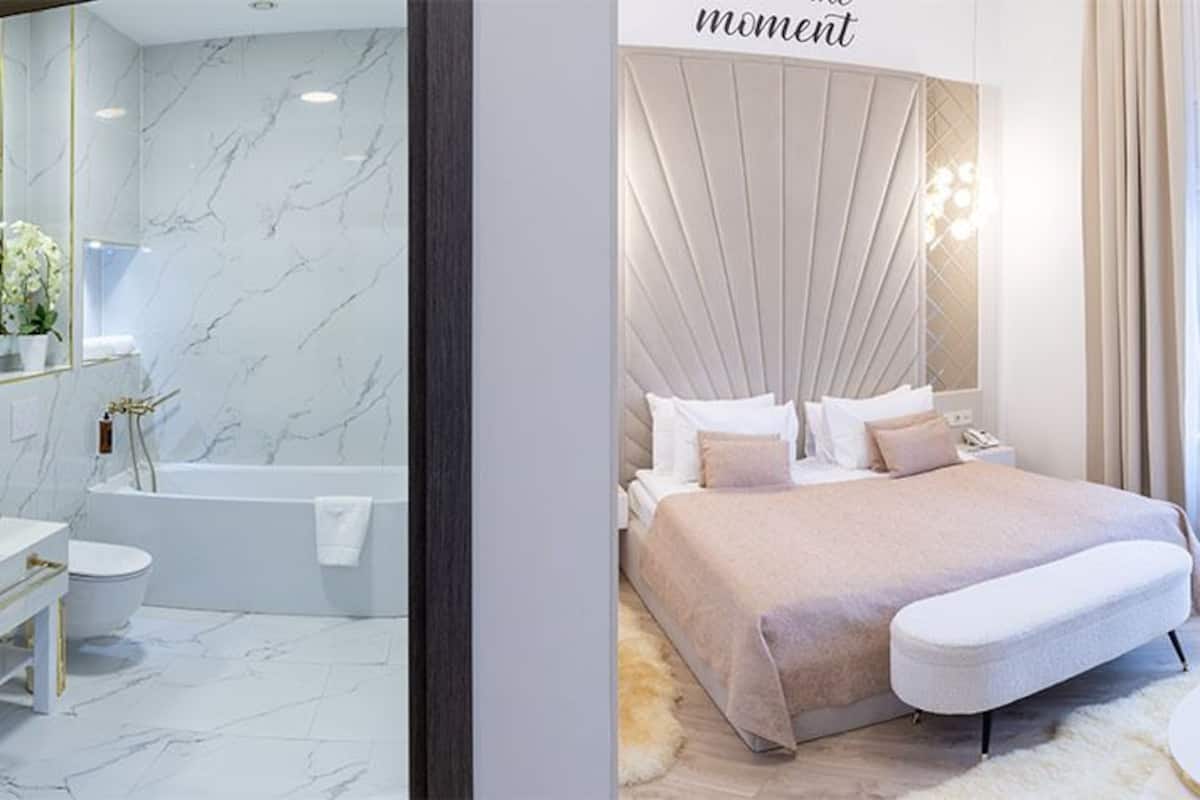 Ett modernt hotellrum med en stor säng, en sittgrupp, ett badrum och utsikt över staden.