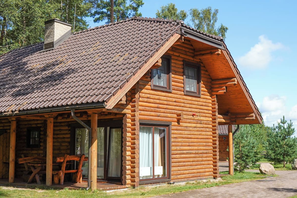 En timmerstuga med ett tak täckt av tegelpannor, en veranda med ett bord och stolar samt en stor skjutdörr av glas.