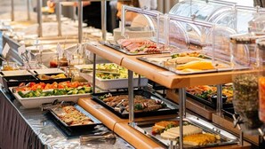Un bufé con diversas opciones de comida, incluyendo carnes, ensaladas y postres, dispuestas en un mostrador con cubiertas de vidrio transparente.