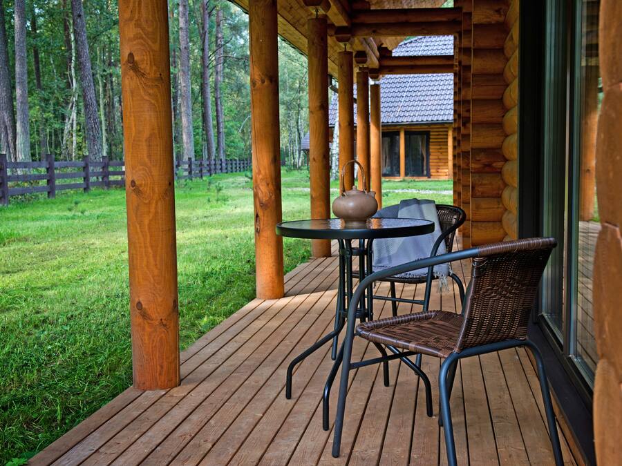 A wooden deck with a table and chair, overlooking a grassy area and a cabin.
