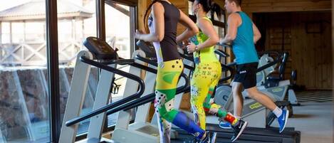 Tres personas corriendo en cintas de correr en un gimnasio con ventanas amplias y detalles de madera.