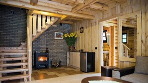 Interior de una cabaña de troncos con chimenea, escalera de madera y un sofá.