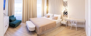 A modern hotel room with a bed, a desk, a chair, a sofa, and a wardrobe.