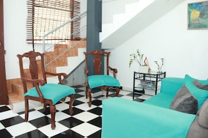 A living room with a checkered floor, wooden chairs with teal cushions, a teal sofa, and a small table with decorative items. - Aarony House (Santo Domingo)