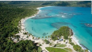 An aerial view of a tropical beach with clear turquoise waters, dense greenery, and a sandy shoreline. - Aarony House (Santo Domingo)