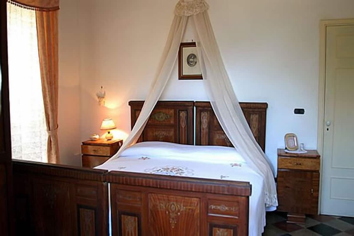 Un dormitorio con una cama de madera, una mesita de noche con una lámpara, una mesita junto a la cama con un reloj y una puerta.