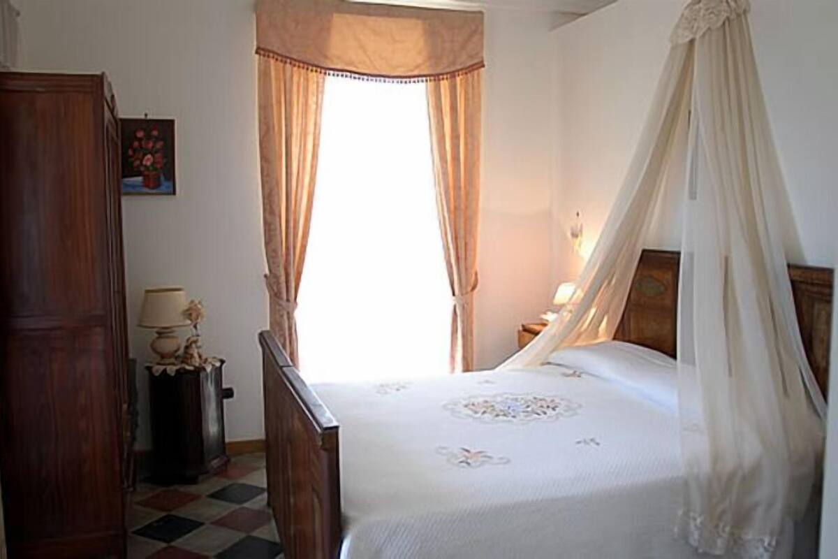Un dormitorio con cama, mesita de noche, lámpara, armario y ventana con cortinas.