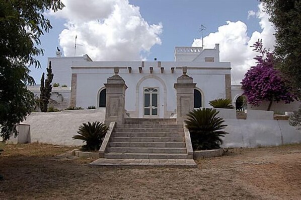 Un edificio blanco con una entrada central, flanqueada por dos columnas, y una escalera que conduce a ella.