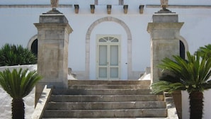 Unos escalones de piedra conducen a un edificio blanco con un arco central y dos columnas a cada lado.
