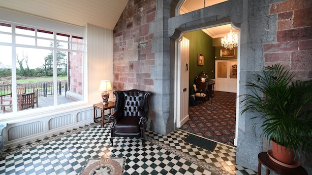 A room with a checkered floor, a fireplace, a large window, and a view of the outdoors. - Glenduff Manor House (Tralee)