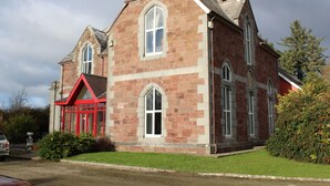A large, red-brick building with a prominent central window and a smaller window on the side. - Glenduff Manor House (Tralee)