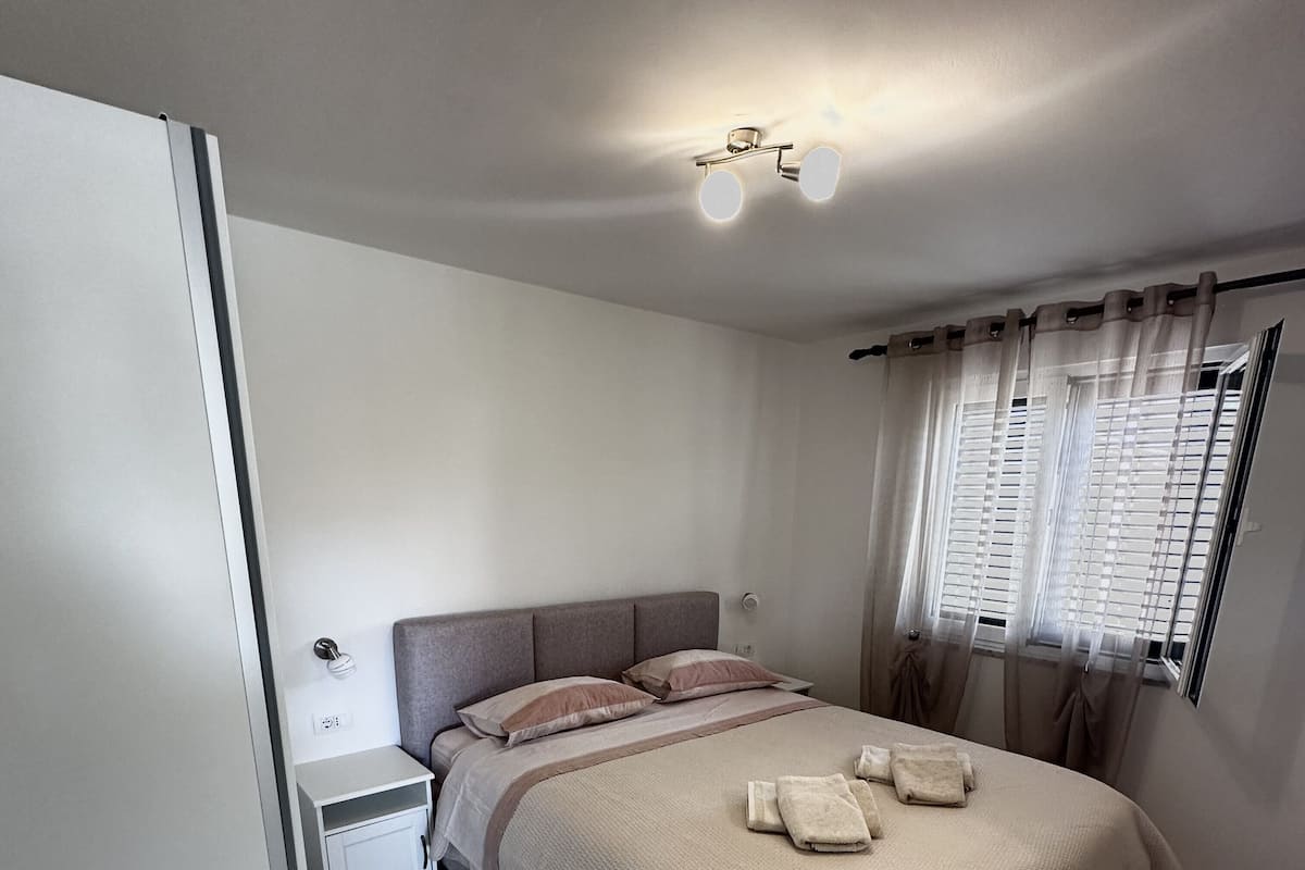 Un dormitorio con cama, mesita de noche y ventana con cortinas.