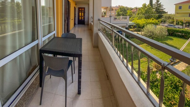 A balcony with a table and chairs, a view of a garden, and a building in the background. - Apartments Malvina (Rovinj)