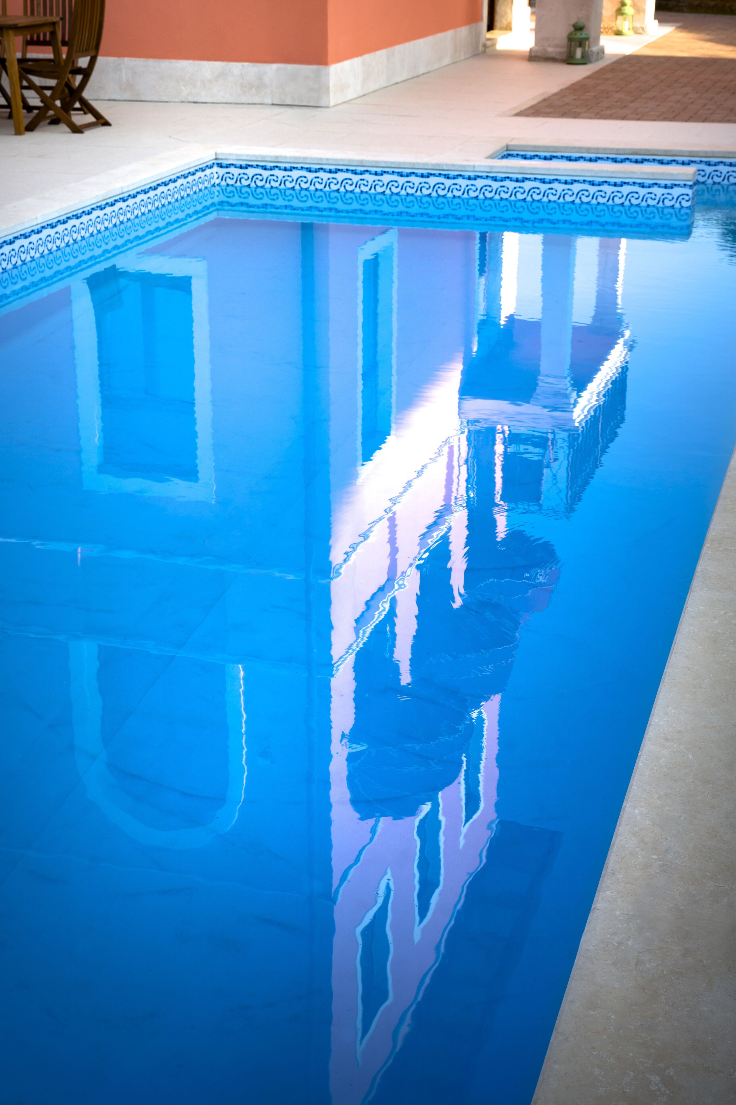 Una piscina cristalina con borde azul y el reflejo de un edificio.