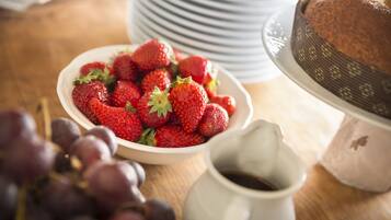 A bowl of strawberries, a cake on a stand, and a pitcher of coffee on a wooden table.