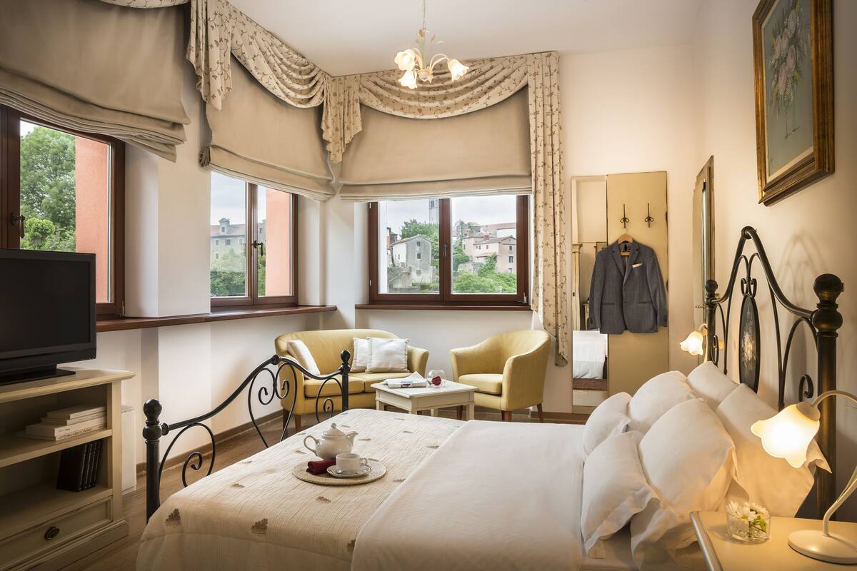 Une chambre d’hôtel équipée d’un lit, d’une télévision, d’un bureau, d’une chaise et d’une fenêtre donnant sur des immeubles.