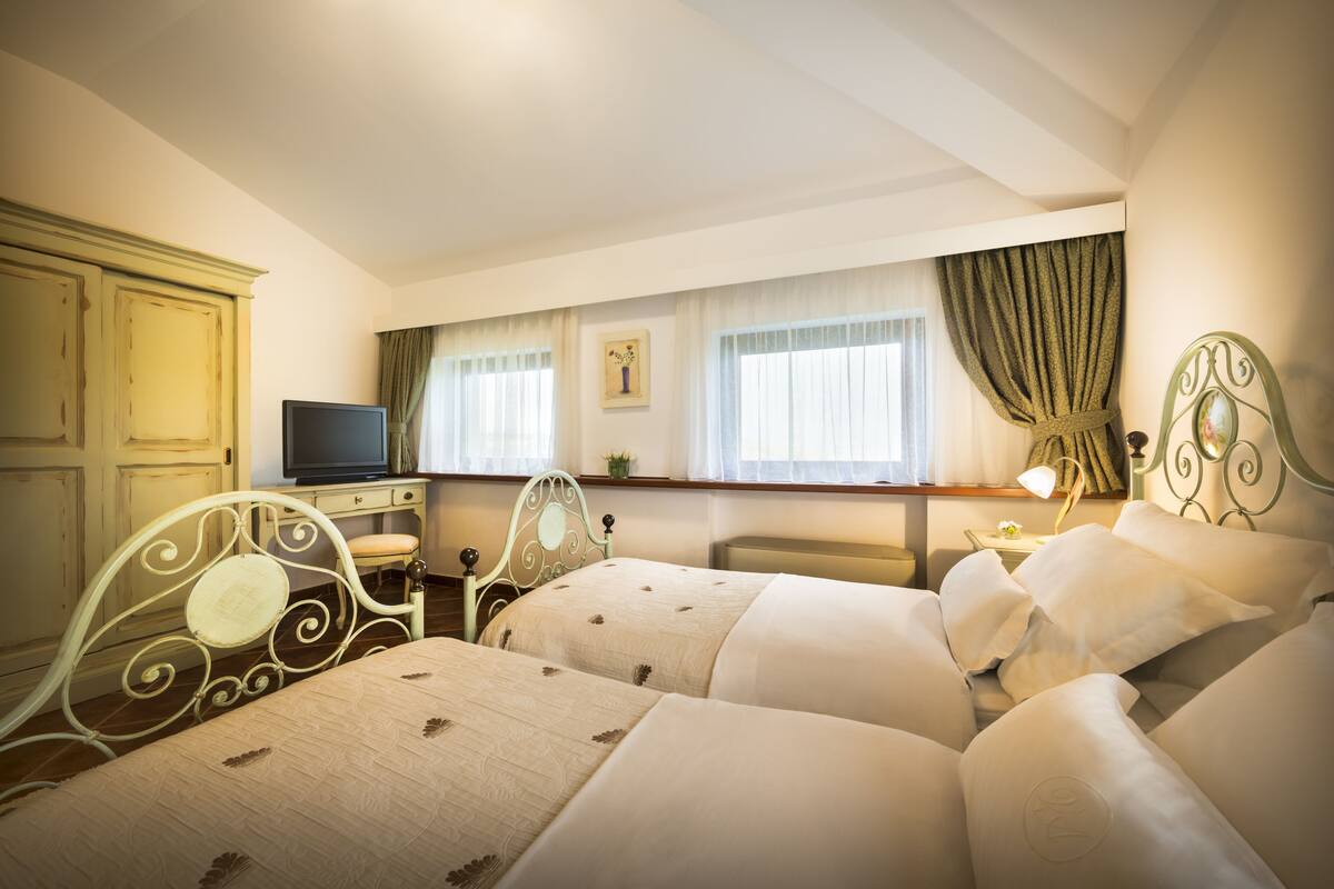 Une chambre d’hôtel avec deux lits, une télévision, un bureau et une fenêtre avec des rideaux.