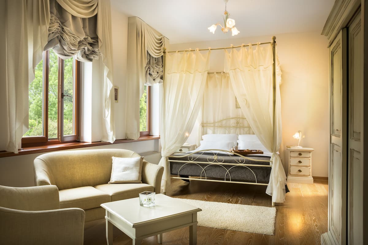 Une chambre à coucher comprenant un lit, une table de chevet, une commode, une chaise et une fenêtre avec des rideaux.