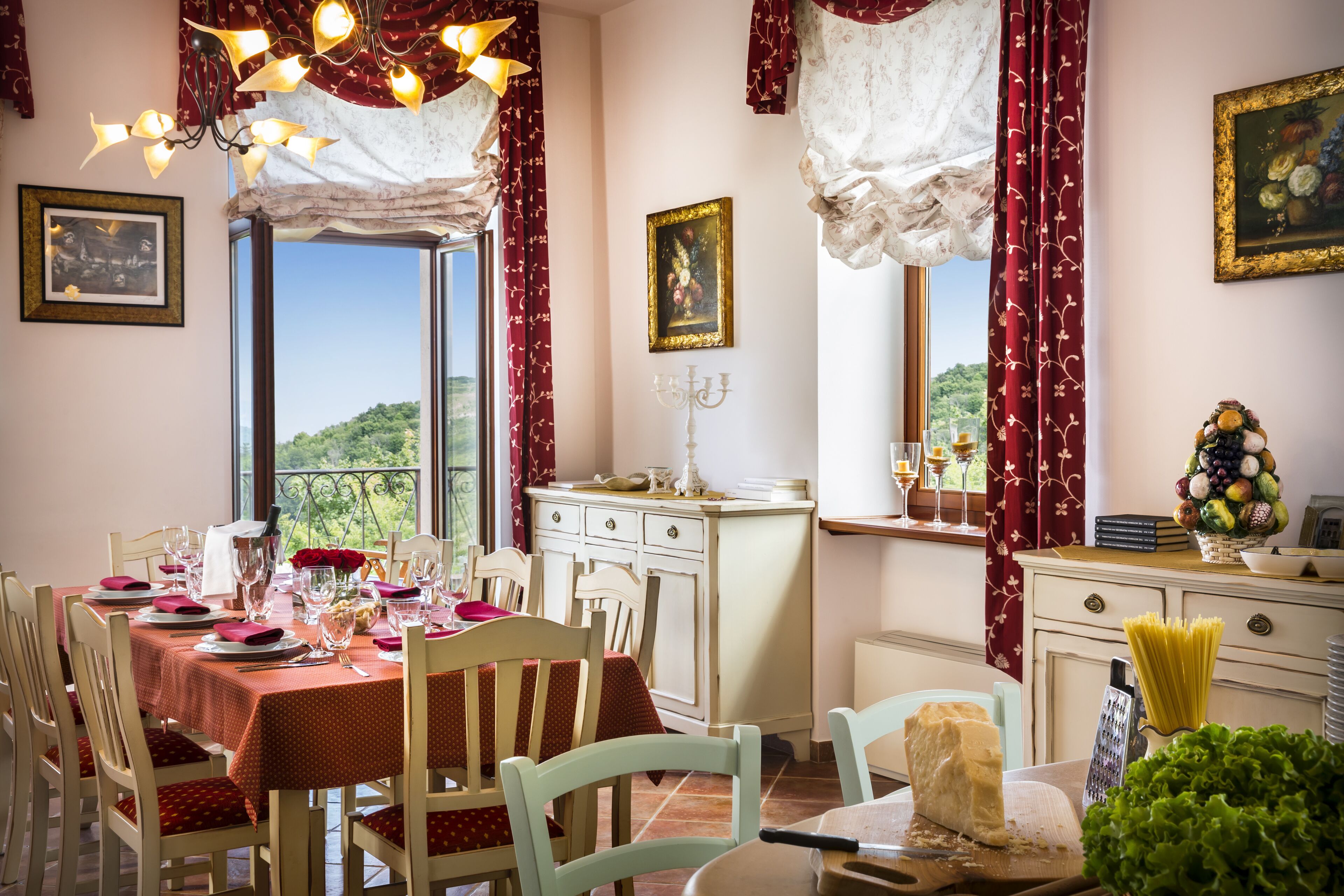 Un coin repas avec une table dressée pour quatre personnes, un lustre et une vue sur la verdure environnante.