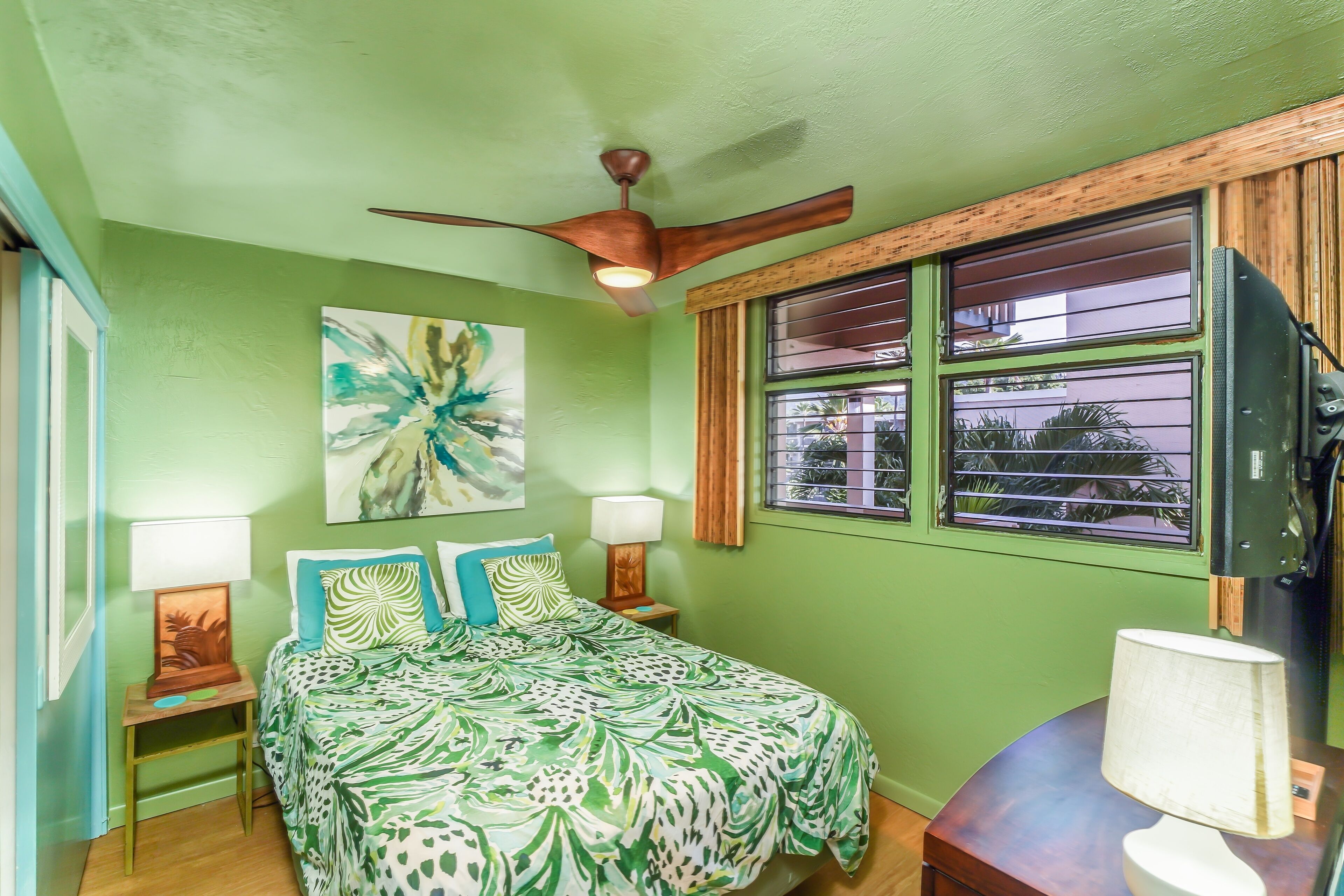 A room with a bed, a ceiling fan, a window with bars, and a painting on the wall.