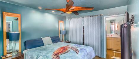 A bedroom with a bed, a ceiling fan, a nightstand, a lamp, a mirror, a window with curtains, and a heater.