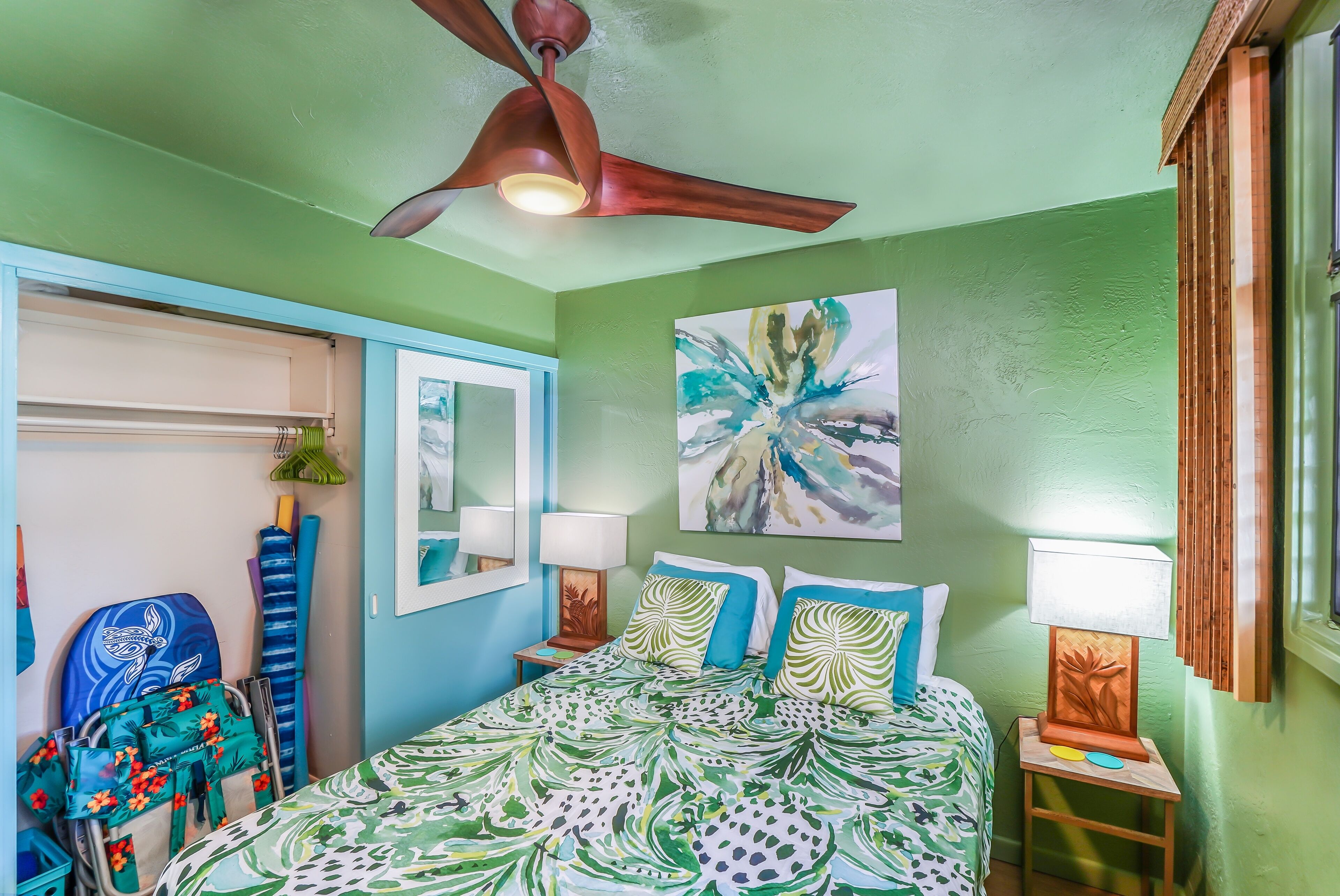 A room with a bed, a ceiling fan, a wall painting, and a window with curtains.
