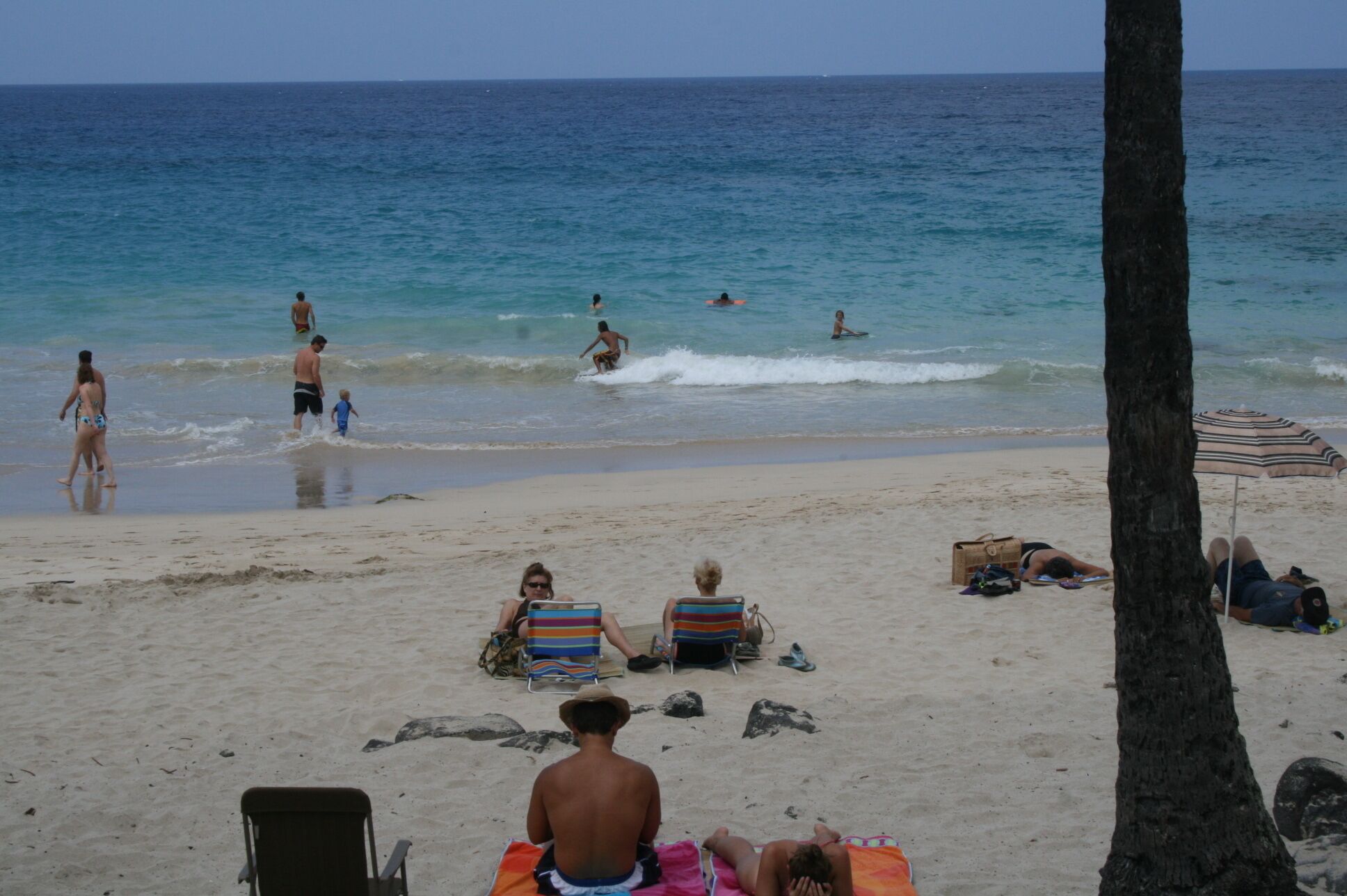Una playa con gente tomando el sol y nadando. Hay sillas de playa y una sombrilla.