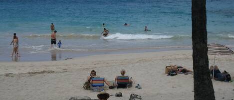 Una playa con gente tomando el sol y nadando. Hay sillas de playa y una sombrilla.