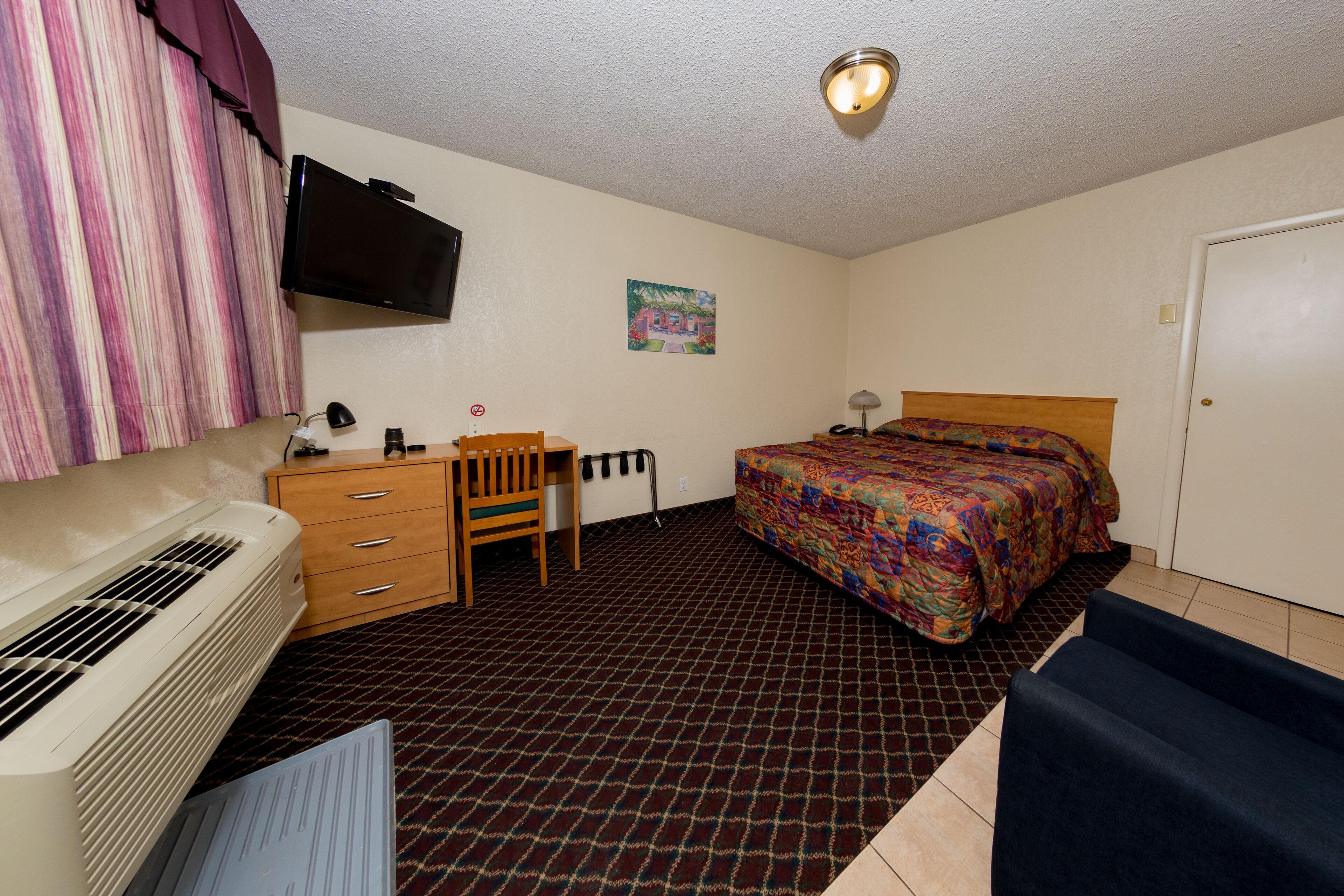 A hotel room with a bed, a desk with a chair, a television, and a heater.