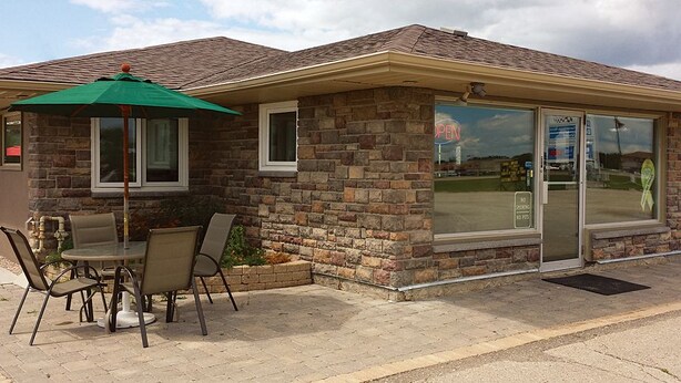 Un petit bâtiment en briques doté d’un patio comprenant une table et des chaises, un parasol vert et une porte d’entrée en verre.